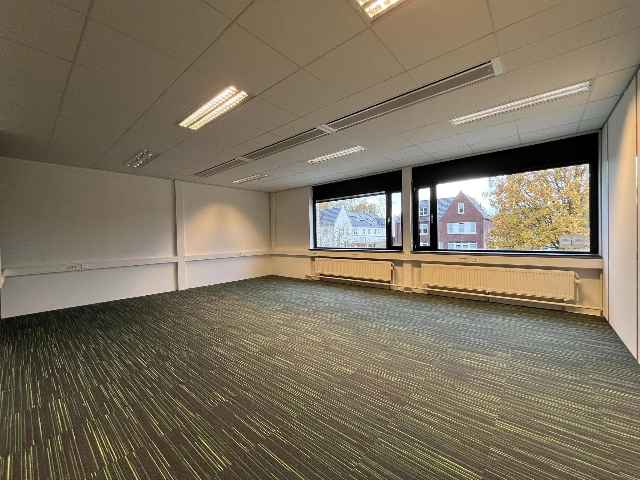 Leeg kantoor met tapijtvloer en grote ramen aan de Burgemeester Verderlaan.